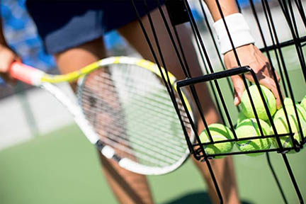 teaching proessional grabbing a ball from a basket of tennis balls